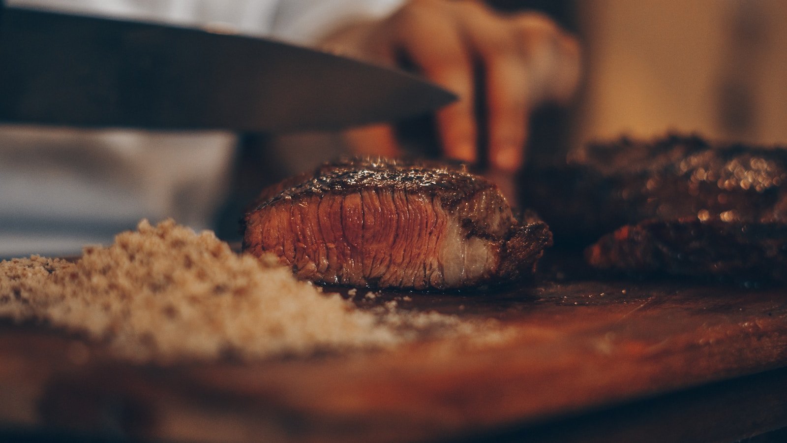 Chef slicing a seared steak on a wooden cutting board