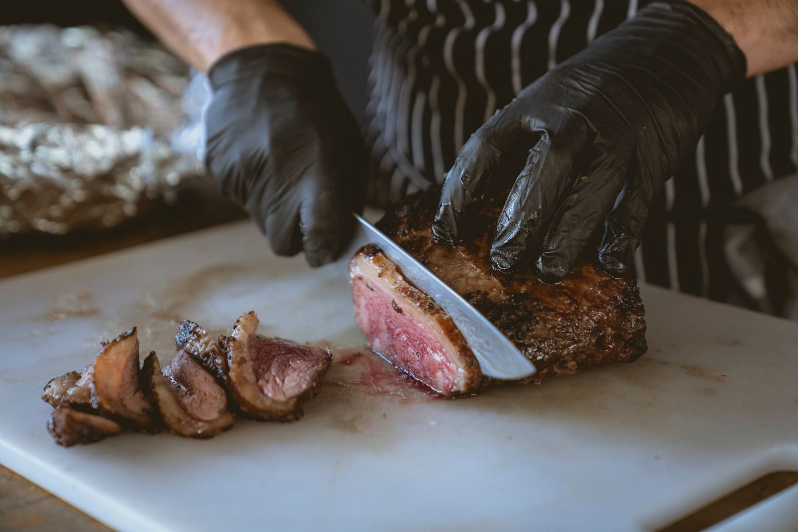 Chef in gloves slicing a cooked steak on a cutting board
