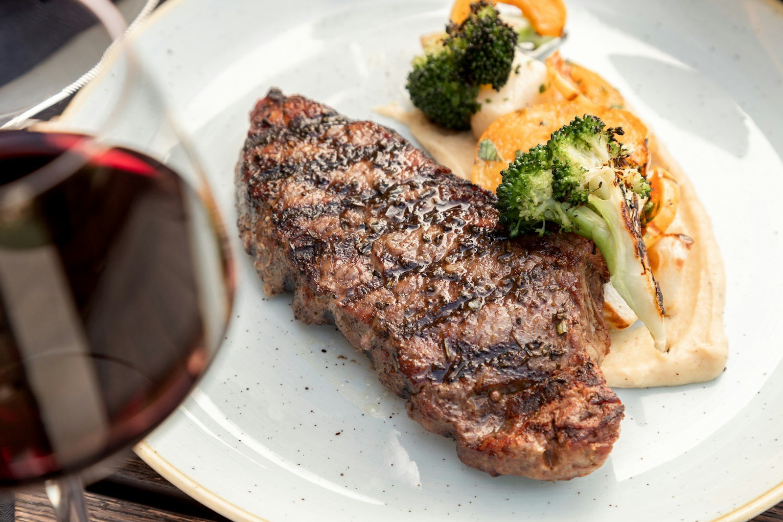 Grilled steak plated with vegetables and a glass of red wine