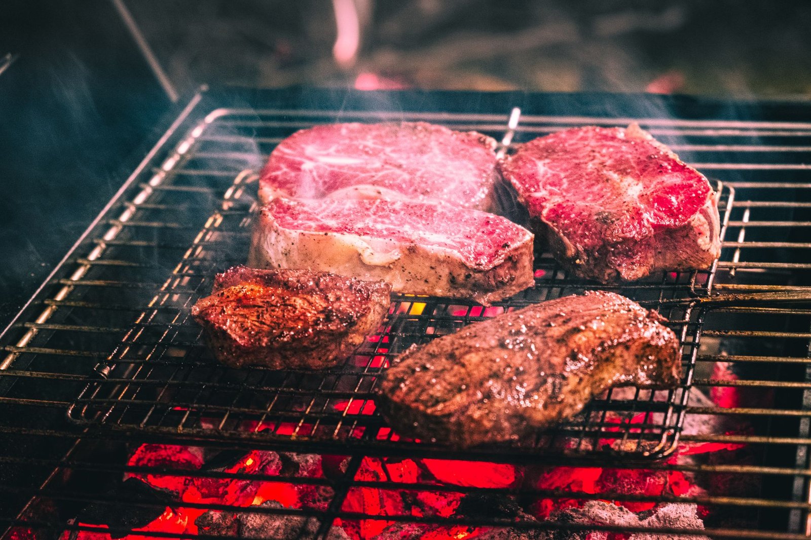 Steaks grilling over hot coals with a red center visible